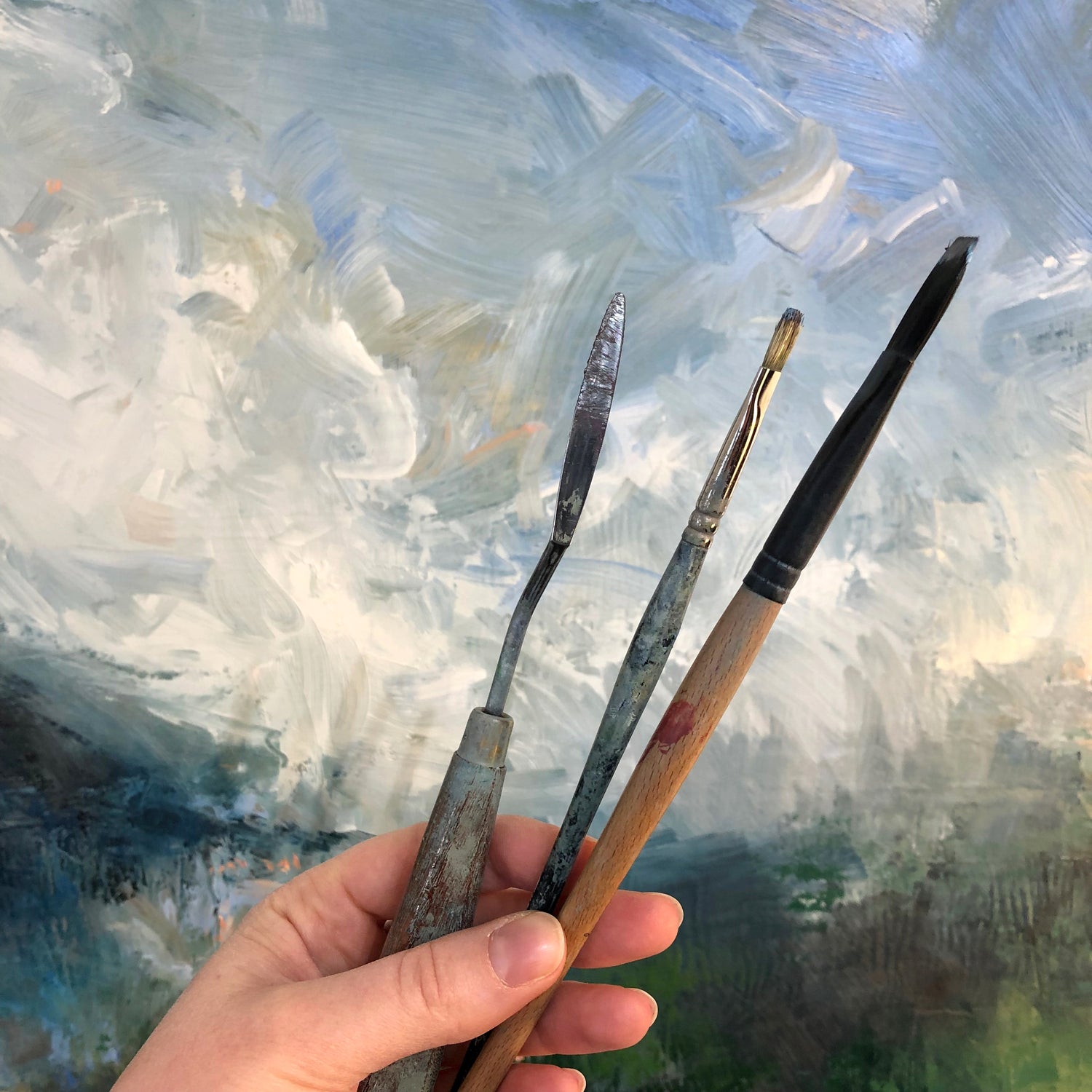 Left hand holding paintbrushes in front of painting